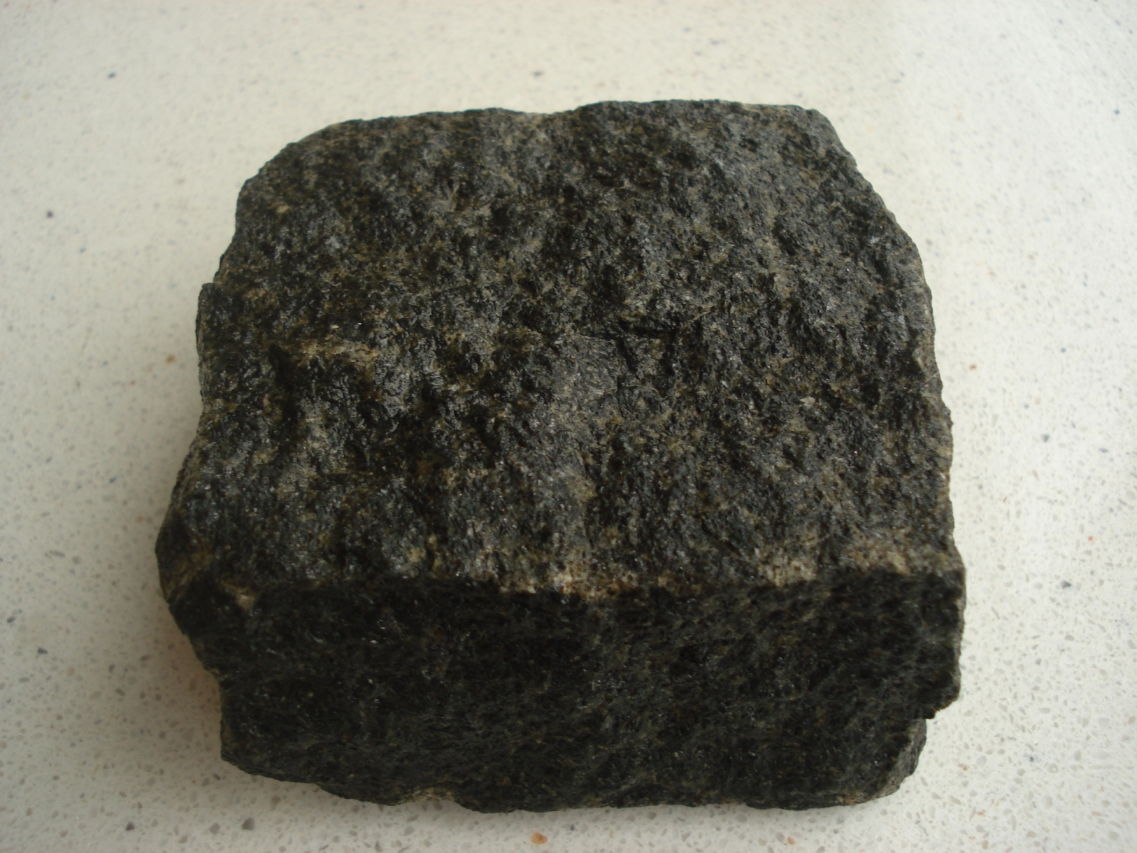 Kostka granitowa o szorstkiej, ciemnej powierzchni na jasnym tle.